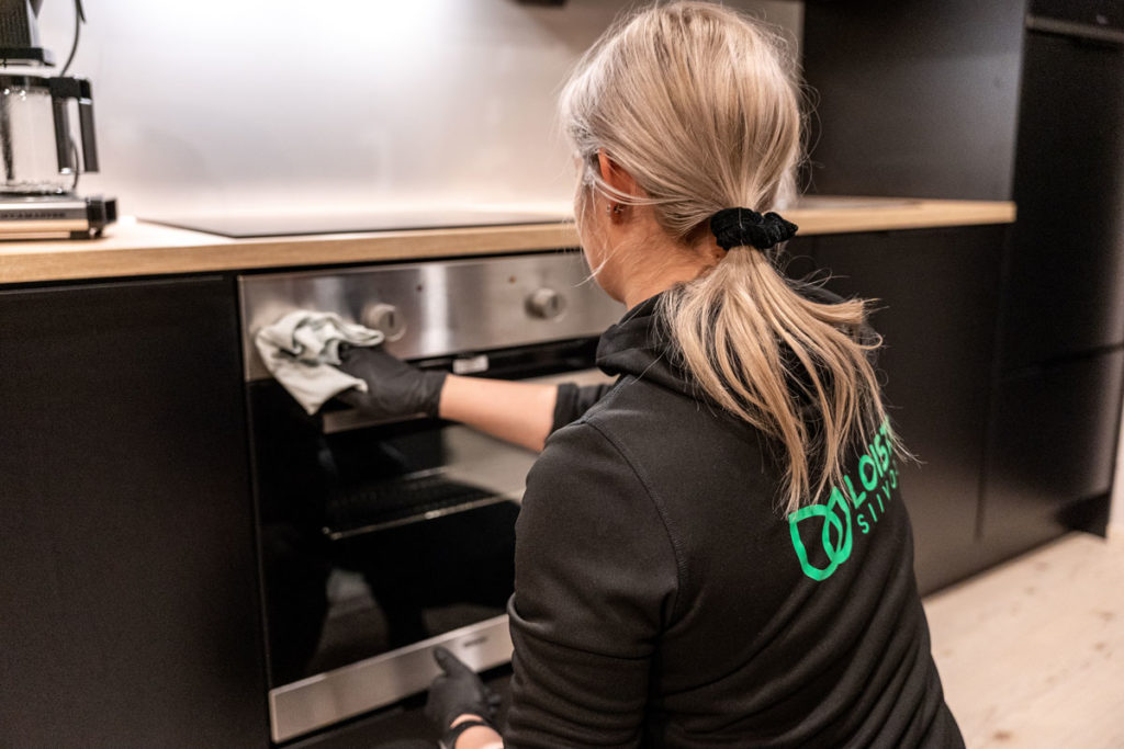 Loiste Siivouksen blogitekstin artikkelikuva, jossa Loisteen siistijällä meneillään keittiön lieden puhdistus. Blogi antaa vinkkejä keittiön siivoukseen.